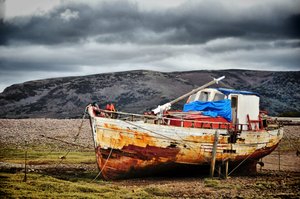 Image of a rusted boat on land in a mountainous landscape.