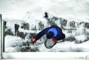 Person spreading chemical on icy surface to melt ice, illustrating increased surface area for reaction