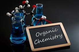 Laboratory glassware and molecular models with 'Organic Chemistry' written on a chalkboard