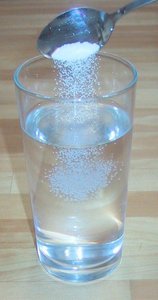 A spoon of salt being added to a glass of water, representing a homogeneous mixture (solution)
