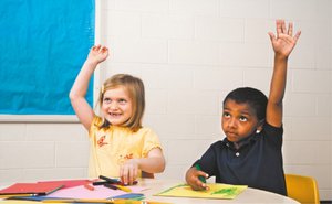 Two children in a classroom raising their hands, illustrating engagement and development in middle childhood.