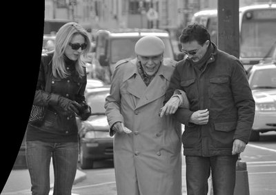 Two people helping an elderly person cross the street